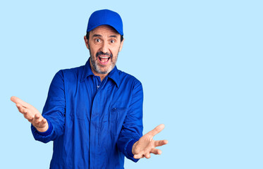 Middle age handsome man wearing mechanic uniform smiling cheerful with open arms as friendly welcome, positive and confident greetings