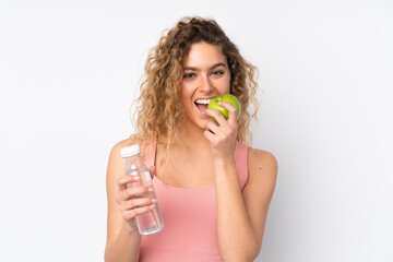 Young blonde woman with curly hair isolated on white background with a bottle of water and eating an apple