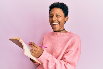 Young african american girl reading and writing book winking looking at the camera with sexy...