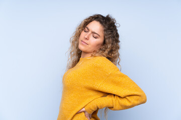 Young blonde woman with curly hair isolated on blue background suffering from backache for having made an effort