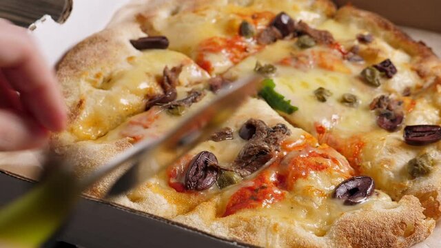 Cut and Take one piece of Fresh baked italian pizza Alla Putanesca in cardboard box on table