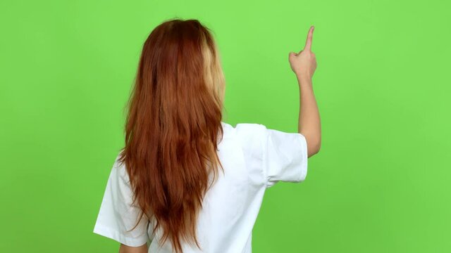 Young blonde teenager girl with stewardess uniform pointing back with the index finger over isolated background. Green screen chroma key