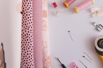 Stacked folded fabrics next to some tailor useful accessories on a white background.