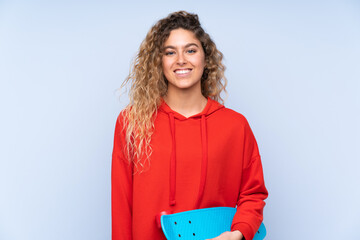 Obraz premium Young blonde woman with curly hair isolated on blue background with a skate