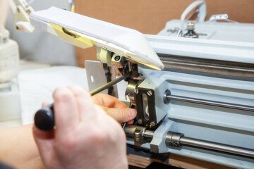 Female hands with a screwdriver repair the shuttle of the sewing machine.
