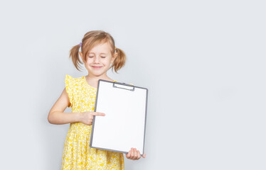 Little Caucasian girl holding a clipboard with a blank paper with copy space