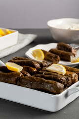 Yaprak sarmasi is a traditional Turkish dish made by wrapping rice stuffing with grape leaves. Served in porcelain tray with lemon slices and a cup of yogurt for dipping. Angled vertical view