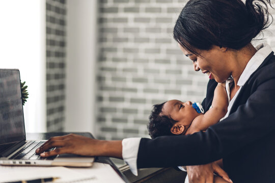 Portrait of african american black mother relaxing using technology of laptop computer with black baby while sitting on table.Young creative african woman working at home.work from home concept