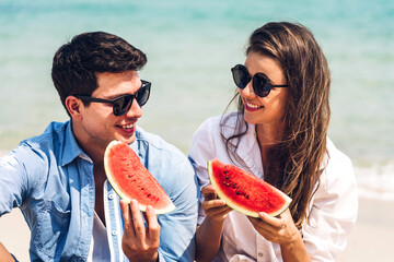 Romantic lovers young couple relaxing holding and eating a slice of watermelon on the tropical beach.Summer vacations