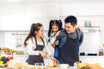 Portrait of enjoy happy love asian family father and mother with little asian girl daughter child having fun cooking food together with baking cookie and cake ingredient on table in kitchen