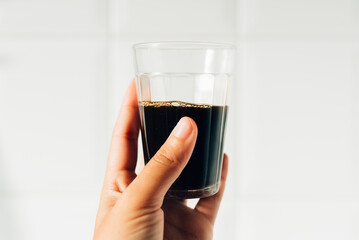 Detalhe de uma pessoa segurando um copo americano (copo lagoinha) com café preto