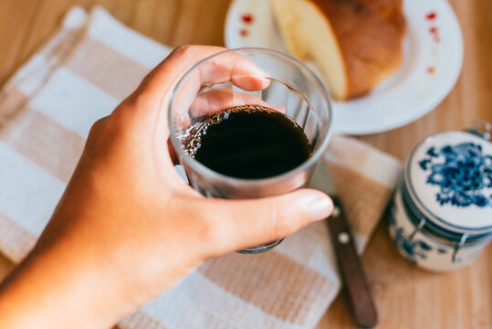 Mulher segurando copo americano (copo lagoinha) com caf&eacute; e uma mesa de caf&eacute; da manh&atilde; atr&aacute;s