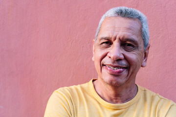 Close up portrait older Hispanic man leaning against wall and staring