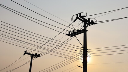 Silhouette of the transmission line on the pole. Placing electrical wiring and connecting transmission lines on poles against the orange sunset background with copy space. Selective focus