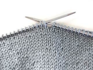 Knitting on knitting needles. Gray woolen fabric on knitting needles on a white background