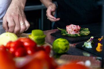 mains en train de préparer une entrée colorée avec des tomates floues en avant plan