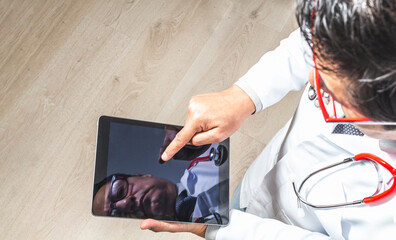 Top view of a doctor in a white coat, tie and stethoscope working on his tablet