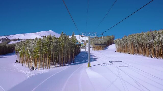 Rearview of riding a ski lift or chairlift filled with skiers and snowboarders for a fun winter day at a ski resort in the Rocky Mountains