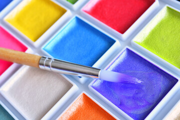 A close up image of brightly colored water paints and paint brushes.  