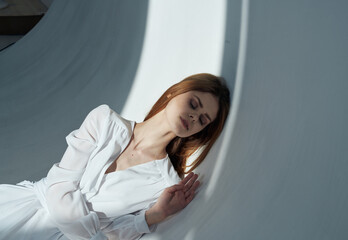 Fototapeta premium Red-haired Woman in a white dress In a bright room side view and a falling shadow
