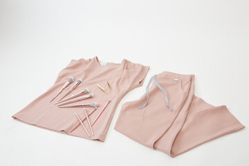 set of make-up brushes and tweezers set on a surgical pink uniform on a white background