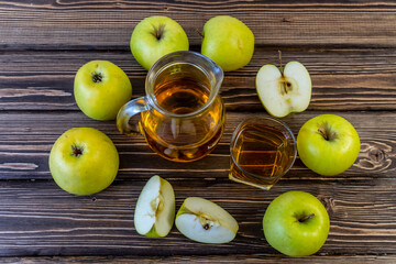 Green apples and jug with glass with apple juice on wooden background