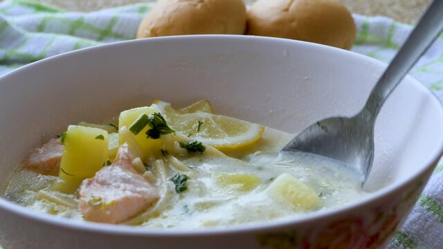 Soup with noodles, boiled potatoes, pieces of red fish. Delicious homemade dish in white bowl with spoon. Ingredients, spices and vegetables