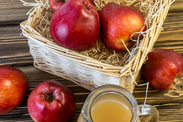 Red apples in a basket and apple juice in a jug on a wooden table