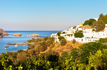 Greece. Rhodes Island. White medieval houses in historic part of the ancient Lindos town on hill above the blue water of the sea bay at sunset. Beautiful seascape. Summer travel and seaside hilidays