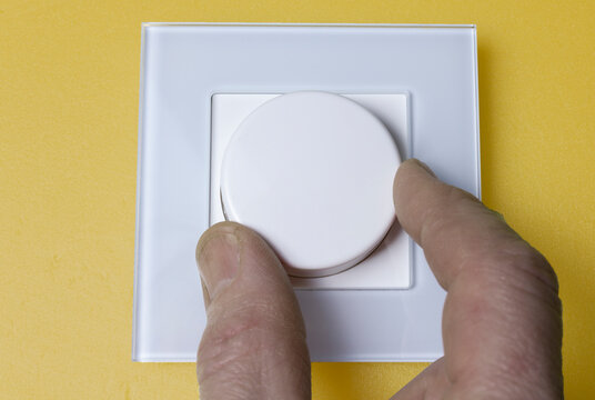 hand turns the white dimmer knob, on the yellow wall