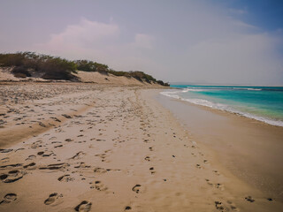 Hot day on the beach of Sal Rei, Cape Verde. Footprints in the sand, bright turquoise water and tropical climate. Selective focus on the texture, blurred background.