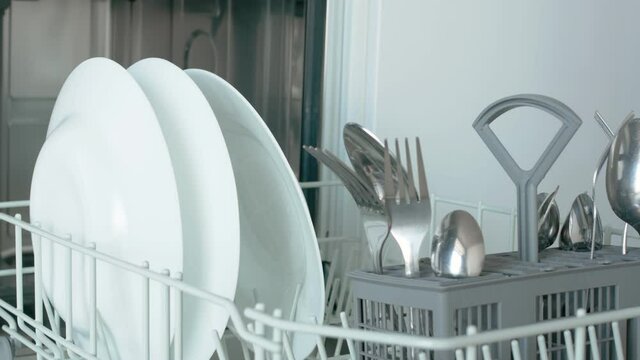 From the bottom drawer of the dishwasher, take out the table pasuda, a round glass bowl, several white plates and a tray with forks and spoons. Close-up