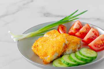 Fried breaded fish fillets withcucumper ant tomatoes served on a plate close up