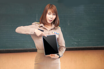Thai teacher in uniform holding and pointing at tablet to her face smiling