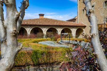 Obraz premium Monastery garden view with well with a rope, well maintained plants and typical church architecture. Meteora, Greece, sunny early spring day landscape