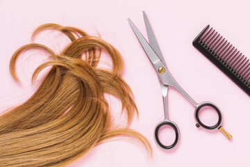 Scissors, a comb and a cut strand of blond female childrens hair on a pink background, top view. Hairdressing concept