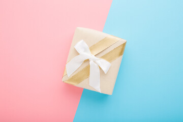 Beige paper gift box with white ribbon on light pink blue table background. Pastel color. Closeup. Congratulation concept. Top down view. Two sides.