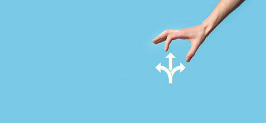 Male hand holding icon with three directions icon on blue background. Doubt, having to choose between three different choices indicated by arrows pointing in opposite direction concept. Ways