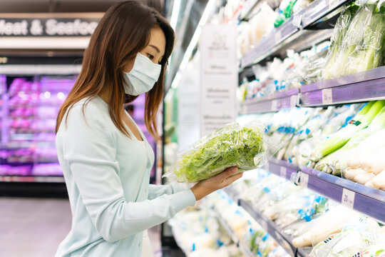 Young Asian Woman Shopping In Supermarket And Wearing Medical Face Mask. Girl Choosing Products  And Reading Labels.