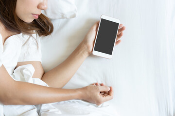 Top view portrait of a tired traveler woman sleeping in bed with mobile phone in hand. Social Addict concept. copy space