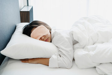 Closeup of happy young Asian woman in sleeping mask sleep in comfortable white bed in the morning.