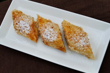 Homemade baklava on white rectangle plate on brown tablecloth. Turkish home baked sweet with sesame on top.