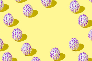 Creative Easter pattern made of natural white eggs with purple stickers on a yellow background. Minimal holiday or spring concept. Copy space.
