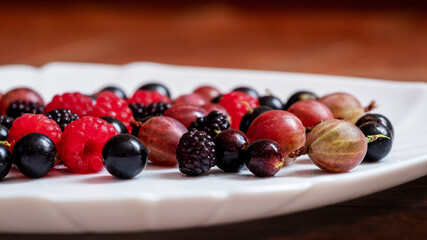 Assorted berries of raspberries, gooseberries, currants on a white plate