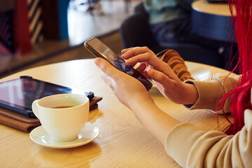 Female hands are typing text messages on a cell phone, in a cafe over a cup of coffee, close-up.