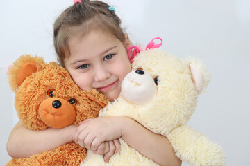 A little blonde girl with her favorite toys, she is happy. In her hands are two large teddy bears