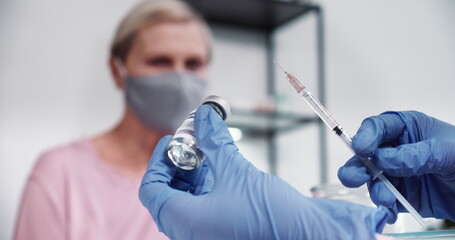 Super close-up, hand of doctor woman in blue protection glove holding syringe and vaccine flask for...