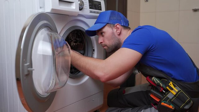 Working man plumber repairs a washing machine in home. Washing machine installation or repair. plumber connecting appliance