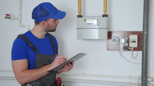 Man in uniform writes down the gas meter reading in a notebook.