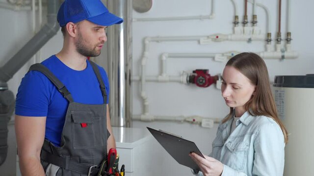 A female client signs a bill from a male plumber standing in the boiler room